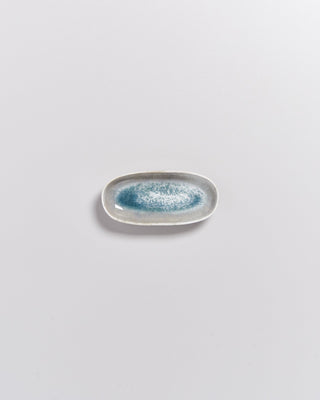 Kleiner, ovaler Teller mit blau-weißer Glasur auf grauem Hintergrund.