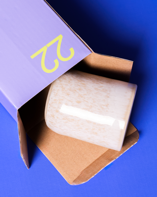 Ein beige Keramik-Objekt ragt aus einem lila Karton mit der gelben Nummer 22 auf blauem Hintergrund.
