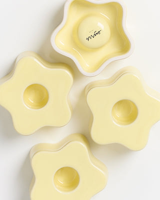 Vier gelbe, blumenförmige Keramikschalen, eine davon mit einem kleinen Schriftzug im Inneren.