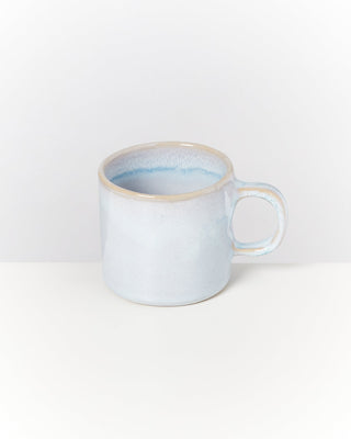 Helle, handgefertigte Keramiktasse mit blau-weißem Farbverlauf auf einem weißen Hintergrund platziert.