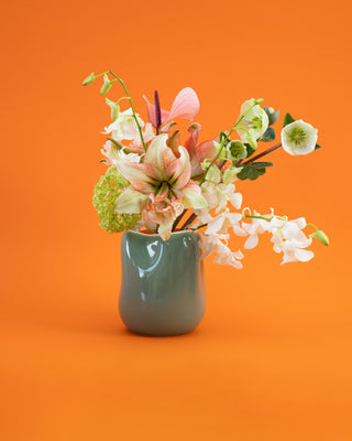 Blumenarrangement in einer grünen Vase vor orangenem Hintergrund.