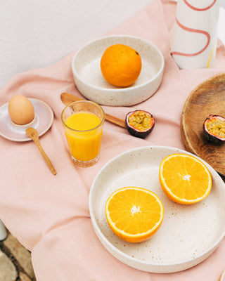Ein Tisch mit einem Ei, einem Glas Orangensaft, einer Orange, einer offenen Passionsfrucht und Orangenhälften auf Tellern.