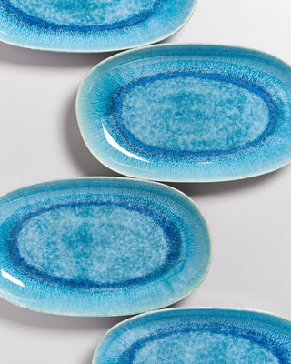 Vier ovale, blaue Teller mit einem aquarellähnlichen Design liegen auf einer weißen Oberfläche.