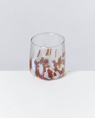 Ein Glas mit braunen und weißen Mustern steht auf einem weißen Tisch vor einem grauen Hintergrund.