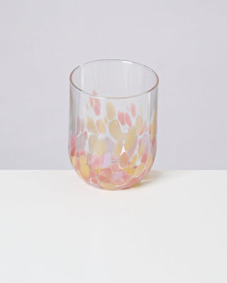 Ein Glas mit bunten Punkten in Rosa und Gelb steht auf einem weißen Tisch vor einem neutralen Hintergrund.