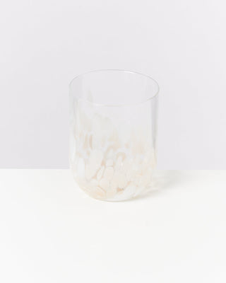 Ein transparentes Glas mit einem Muster aus weißen Flecken steht auf einer weißen Oberfläche vor weißem Hintergrund.