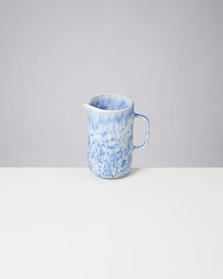 Blauer Keramikkrug mit Marmormuster auf weißem Tisch vor grauem Hintergrund.