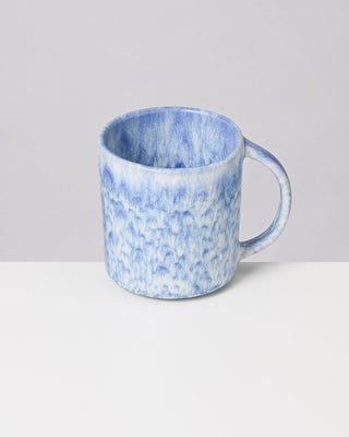 Blauer und weißer Keramikbecher mit Marmormuster auf weißem Tisch vor grauem Hintergrund.
