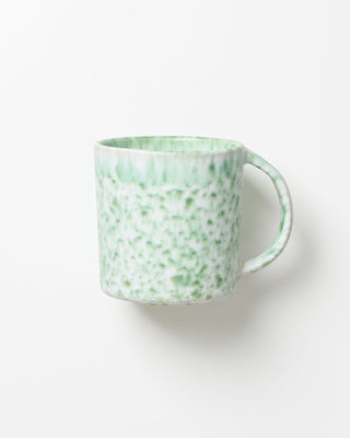 Grüne Tasse mit fleckigem Muster auf weißem Hintergrund.