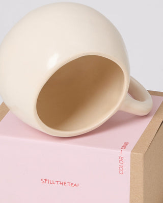 Beige Tasse auf pinkem Karton, der mit "Spill the Tea!" beschriftet ist.