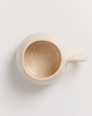 Beige Tasse aus Keramik von oben fotografiert auf weißem Hintergrund.