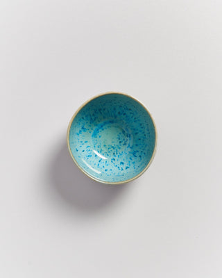 Schale mit türkis-blauem Muster auf weißem Hintergrund von oben fotografiert.