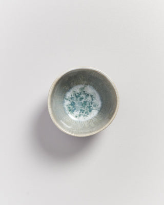 Kleine graue Keramikschale mit blau-weißem Muster auf hellem Hintergrund.