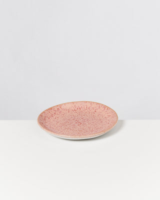 Ein rosa Keramikteller mit gesprenkeltem Muster auf einem weißen Hintergrund.