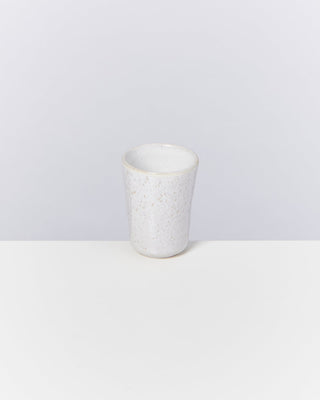 Weißer, texturierter Keramikbecher auf einem weißen Tisch vor grauem Hintergrund.