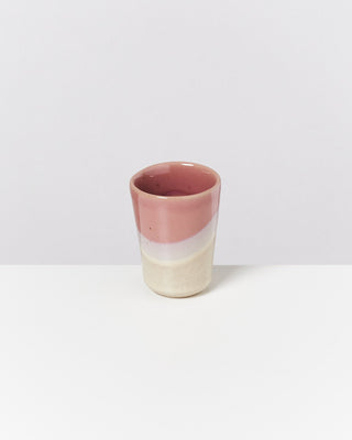 Ein kleiner, dreifarbiger Keramikbecher mit rosa, weißem und beigem Farbverlauf steht auf einer weißen Oberfläche.