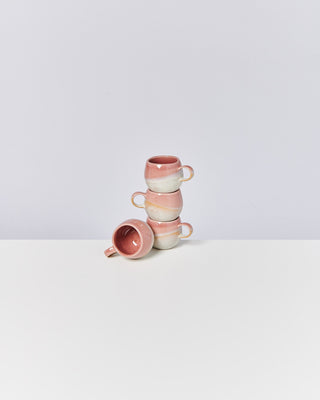 Vier stapelbare, rosa-weiße Keramiktassen auf einem weißen Tisch vor einem hellen Hintergrund.