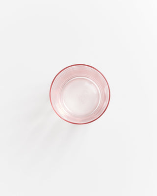 Ein leeres, transparentes Glas mit leichtem rosa Schimmer auf einem weißen Hintergrund.