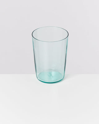 Ein klares Glas steht auf einer weißen Oberfläche vor einem hellgrauen Hintergrund.