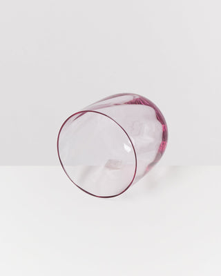 Ein durchsichtiger, rosa Glasbecher liegt seitlich auf einer weißen Oberfläche.
