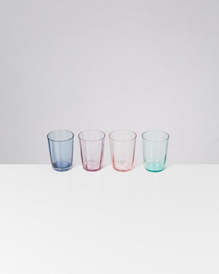 Vier bunte Gläser in Blau, Rosa, Hellrosa und Hellgrün stehen nebeneinander auf einem weißen Tisch.