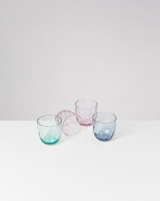 Drei bunte Trinkgläser und ein umgefallenes Glas auf weißem Hintergrund.