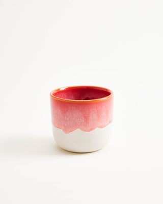 Kleine Keramiktasse mit rotem oberen Rand und weißem Boden auf weißem Hintergrund.