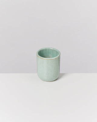 Ein hellgrüner Keramikbecher steht auf einer weißen Oberfläche vor einem grauen Hintergrund.