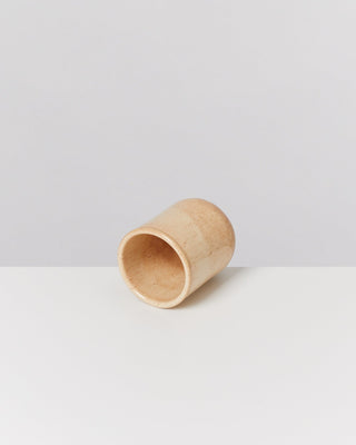 Holzbecher liegt seitlich auf einem weißen Tisch vor einem neutralen Hintergrund.