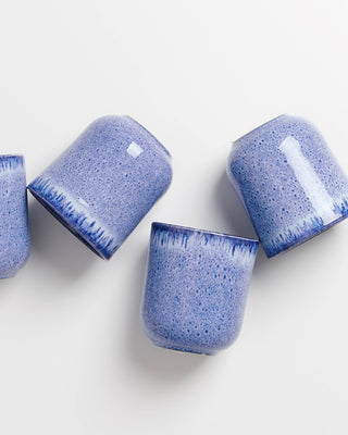 Vier blaue, keramische Becher mit gesprenkeltem Muster liegen auf einer weißen Oberfläche.
