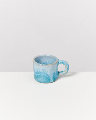 Eine kleine, blaue Keramiktasse mit Henkel steht auf einem weißen Hintergrund.