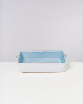 Rechteckige Keramik-Auflaufform mit blauer Innenseite steht auf einem weißen Tisch vor grauem Hintergrund.