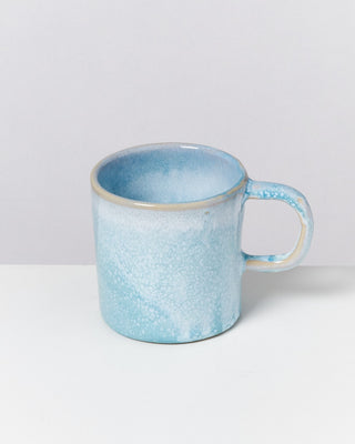 Eine hellblaue Keramiktasse mit einem fleckigen Muster steht auf einer weißen Fläche.