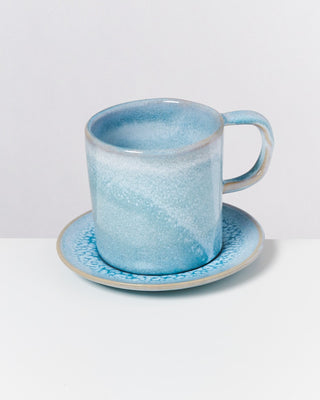 Blaue Keramiktasse mit passender Untertasse auf weißem Hintergrund.