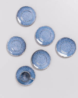 Sechs blaue Keramikteller, einer mit einer Tasse, sind kunstvoll auf einer hellen Oberfläche arrangiert.