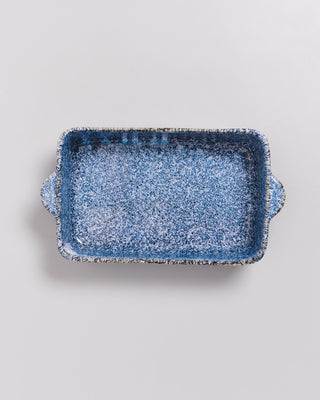 Blaue Keramikauflaufform mit gesprenkeltem Muster und Griffen auf einem hellgrauen Hintergrund.