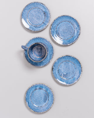 Fünf blaue Untertassen und eine Tasse mit Untertasse sind auf einer weißen Oberfläche angeordnet.