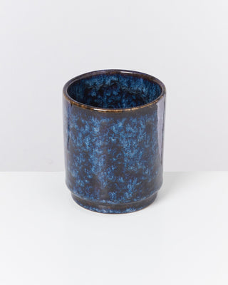 Blauer, zylindrischer Keramikbecher mit dunklem, marmoriertem Muster auf weißem Hintergrund.