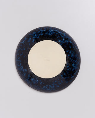 Runder Teller mit blau-schwarzer Glasur und heller, unglasierter Mitte auf grauem Hintergrund.