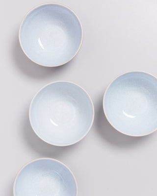 Vier helle, blau-weiße Keramikschalen sind auf einer grauen Oberfläche verteilt angeordnet.