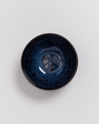 Dunkelblaue, glänzende Keramikschale mit kunstvollem Muster auf hellem Hintergrund.