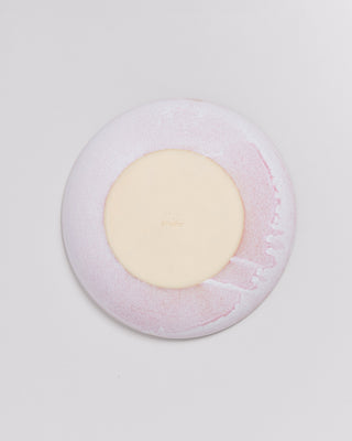 Runder Teller in hellem Rosa und Creme auf weißem Hintergrund.