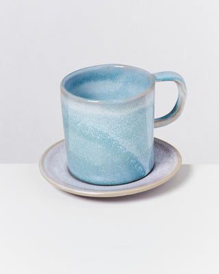 Blaue Keramiktasse mit Unterteller vor hellem Hintergrund.