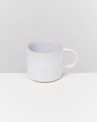 Weiße Keramiktasse mit Henkel auf einem weißen Tisch vor grauem Hintergrund.