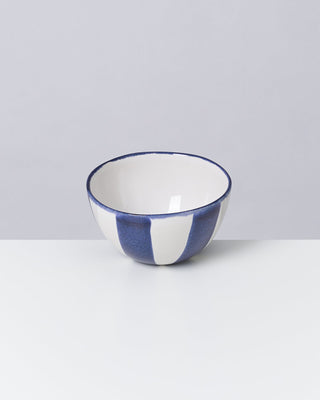 Weiße Keramikschale mit blauen Streifen auf einem weißen Tisch vor grauem Hintergrund.