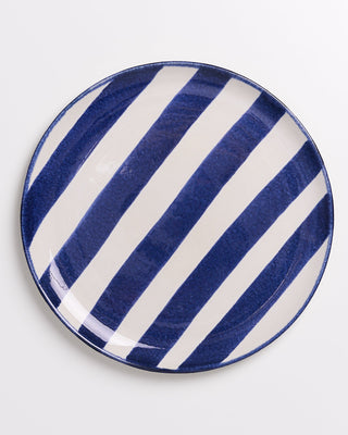 Runder Teller mit diagonalen blauen und weißen Streifen auf weißem Hintergrund.