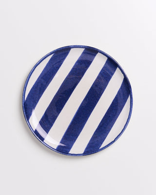 Runder Teller mit diagonalen blauen und weißen Streifen auf weißem Hintergrund.