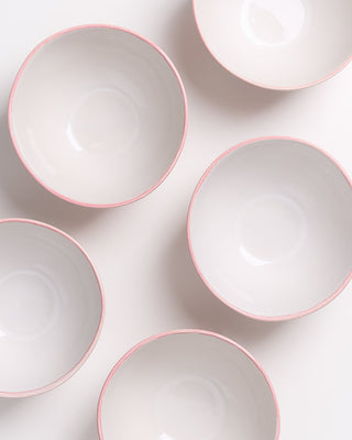 Fünf weiße Schalen mit rosa Rand sind auf einer weißen Oberfläche arrangiert.