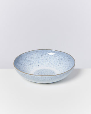 Blaue Keramikschale mit gesprenkelter Oberfläche auf einem weißen Untergrund, vor einem schlichten, grauen Hintergrund.