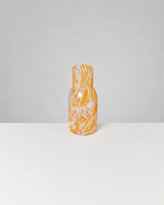 Bunte, orange-weiße Glasvase mit abstrakten Mustern steht auf einem weißen Tisch vor grauem Hintergrund.